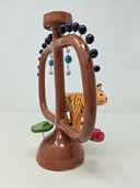 Glossy ceramic sculpture of a brown vessel with a thin center shape and 2 large handles. In front of it is a tiger with some lily pads and red flowers. Dark blue spheres come out of short wire along the top of the handles.