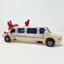 Ceramic sculpture of a white limo with small red devils hanging around it and inside of it, one pops out of the sun roof, the other hangs out and open door and the final is under the car.