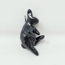 Shiny black ceramic sculpture of a rabbit without any defined facial features and elongated feet. It is attached to a hook.