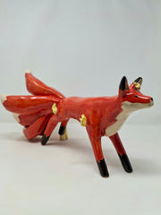 Glossy ceramic sculpture of a red fox with a large tail, composed of 9 different smaller tails. The fox has a small golden flame on its forehead and some more gold flames coming of its body.