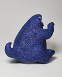 A blue textured dinosaur monster figurine with an open mouth showing white teeth, sitting on a light gray background.