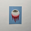 A vertical art print featuring a surreal illustration of a white eyeball with a green iris and red blood-like drips, set against a light blue background, mounted on a textured light gray wall.