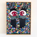 A framed folk art painting of 2 girls with red toned skin, wearing black bunny ears and black dress, they face each other and stand in a dense field of colorful flowers, displayed on a plain white wall.