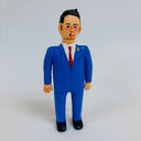 Clay sculpture of a business man, wearing a blue suit with a white shirt, red tie and smoking a cigarette.