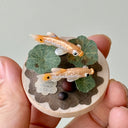 Small sculpture of 2 fish on a wooden base with paper plants and small rocks.