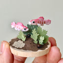 Miniature diorama with two pink fish and green plants held in a hand against a light gray background.