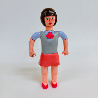 Clay sculpture of a female office worker, with short black hair and bangs, wearing a pink skirt, gray vest and blue short sleeve button up shirt.
