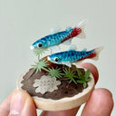 Two small fish figurines on a miniature landscape with a hand holding it.
