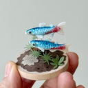 Two small fish figurines on a wooden base held by a hand against a plain background