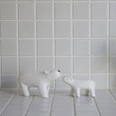 Two white wooden polar bear figurines on a tiled floor with a tiled wall background.