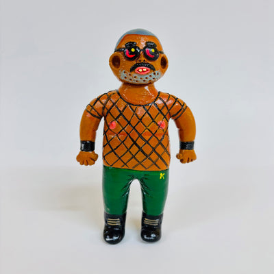 Clay sculpture of a tan man with short hair and black glasses. He wears a black mesh shirt, green pants and black shoes.