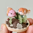 Small decorative scene with two clay fish and plants on a gray background