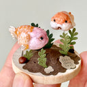 Small wooden ornament with two fish and a rock, held in a hand against a light background.