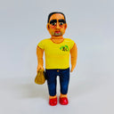 Clay sculpture of a man with very thick eyebrows and tired eyes. He wears a yellow shirt, jeans, red shoes and carries a takeout bag.