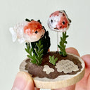 Small decorative sculpture with clay fish and plants held by a hand against a light background