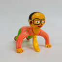 Clay sculpture of a yellow man with glasses and tired, but wide yes, kneeling on the ground with his hands touching the floor and his knees slightly lifted, as though almost doing a pushup.