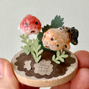 Small sculpture of 2 ranchu goldfish on a wooden base with paper plants.
