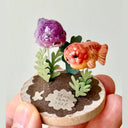 Small decorative piece with two fish and plants on a circular base, held by a hand.