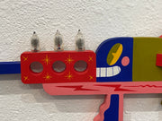 Colorful abstract sculpture with geometric shapes and light bulb-like objects on a textured wall.