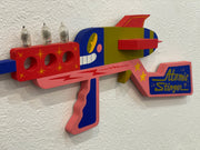 Colorful toy gun with 'Atomic Stinger' branding on a textured white background