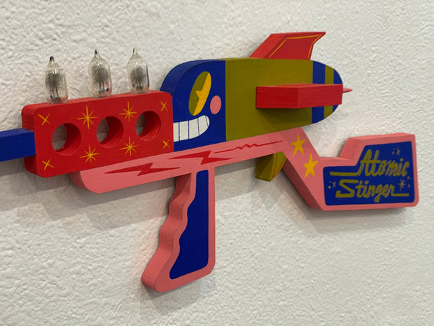 Colorful toy gun with 'Atomic Stinger' branding on a textured white background