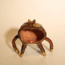 Ceramic sculpture of a brown cat, with 6 very long, thin legs and a giant open mouth, which comprises most of its face and all of its body. It has a tiny tongue and small fangs. The cat has small dot eyes and pointed ears.