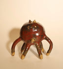 Ceramic sculpture of a brown cat, with 6 very long, thin legs and a giant open mouth, which comprises most of its face and all of its body. It has a tiny tongue and small fangs. The cat has small dot eyes and pointed ears.