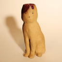 Ceramic sculpture of a tall brown cat, sitting and looking forward with simplistic eyes and a nose. Its head is cut open in a cross section, with blood spilling out.