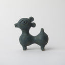 Grayish blue ceramics sculpture of an animal like figure, with a humped body and a head like a deer or lamb, with a large eye and small snout. It has 2 circular ears at the back of its head.