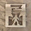 Laser cut design into wood of Big Foot walking through a forest, silhouetted. 