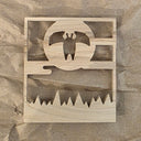Laser cut design into a piece of wood of a flying moth person against a full moon over some trees.
