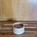 Wooden incense holder with a single incense stick on a wooden surface.