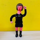 Clay sculpture of a pink woman with short black hair and bangs, wearing a suit top and a mini skirt, both are all black. She wears black boots and has red fishnet tights.