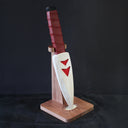 Whittled wooden sculpture of a knife, turned down and onto a stand. The blade of the knife is white with red arrow patterning and the handle is leather bound.