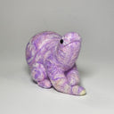 A small handcrafted felted wool animal figurine in a crouched pose, featuring a marbled purple and white color pattern with a small black bead eye, set against a plain light gray background.