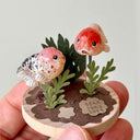 Small sculpture with goldfish and plants held in a hand against a light background