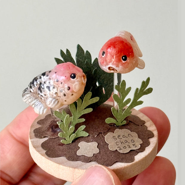Small sculpture with goldfish and plants held in a hand against a light background