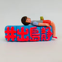 Clay sculpture of an office woman laying down on large blocks with Japanese kanji written on them. She looks very tired or slightly inebriated and holds a cup.