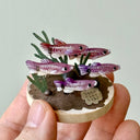 Miniature diorama of fish and plants held in a hand against a light gray background