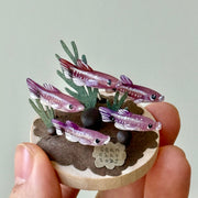 Small model of fish and plants held in a hand against a plain background