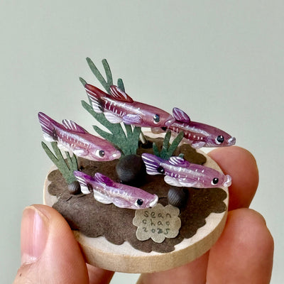 Small model of fish and plants held in a hand against a plain background