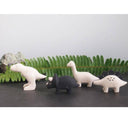 Set of four dinosaur figurines on a dark surface with green leaves in the background