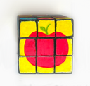 A 3x3 puzzle cube featuring a hand-painted red apple design on a yellow background, set against a plain white backdrop.