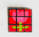 A hand-painted 3x3 Rubik's cube on a plain white background. The top and front faces are decorated with pink and red floral patterns, while the side face is painted lime green.