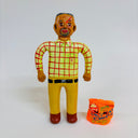 Clay figure of a smiling tan man with large, anime eyes. He wears and yellow with red plaid shirt and yellow slacks. At his feet is a bag of chips with 2 eye holes cut out of it.