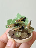 Small sculpture with clay fish and plants held by a hand against a light gray background