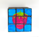 A hand-painted 3x3 Rubik's cube featuring a red strawberry design on the center slice, set against a plain white background.