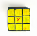 A hand-painted 3x3 Rubik's cube with bright yellow faces, black borders, a small red smiley face in the center.