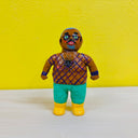 Clay sculpture of a tan man with glasses, standing while wearing a purple mesh top , green pants and yellow boots.