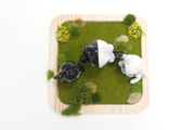 Three cat shaped figurines, with cute, large anime style eyes standing on a wooden tray with fake grass. They all have 2 tails. Seen from overhead.